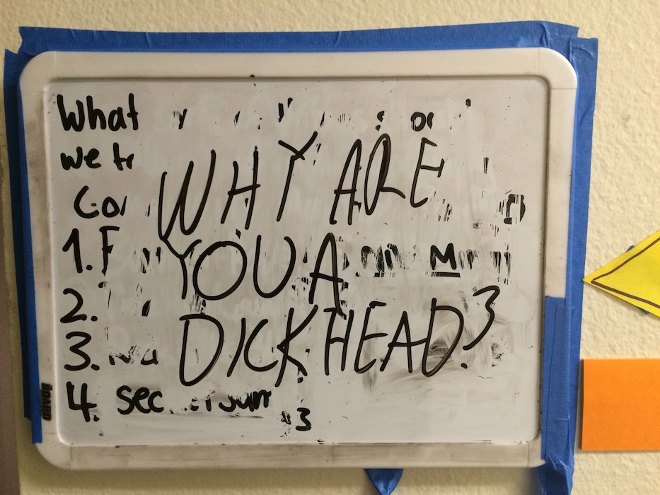Whiteboard with “WHY ARE YOU A DICKHEAD?” written on it